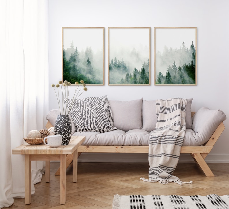 May include: Three framed prints of a misty forest scene with green trees. The prints are hanging on a white wall above a light gray couch with a white and black striped throw blanket.