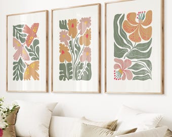 May include: Three framed prints featuring abstract floral designs in shades of pink, orange, and green. The prints are displayed against a white wall.