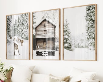 May include: Three framed art prints showing a winter landscape. The prints feature a wooden cabin, reindeer, and snow-covered trees. The frames are made of light-coloured wood, and the overall aesthetic is neutral and serene.
