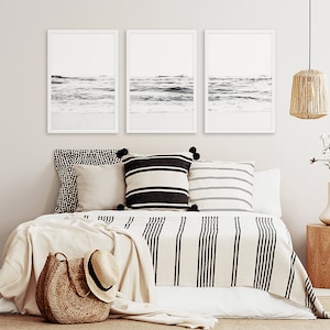 May include: Three black and white framed photographs of ocean waves hanging above a bed with a white and black striped blanket and pillows.