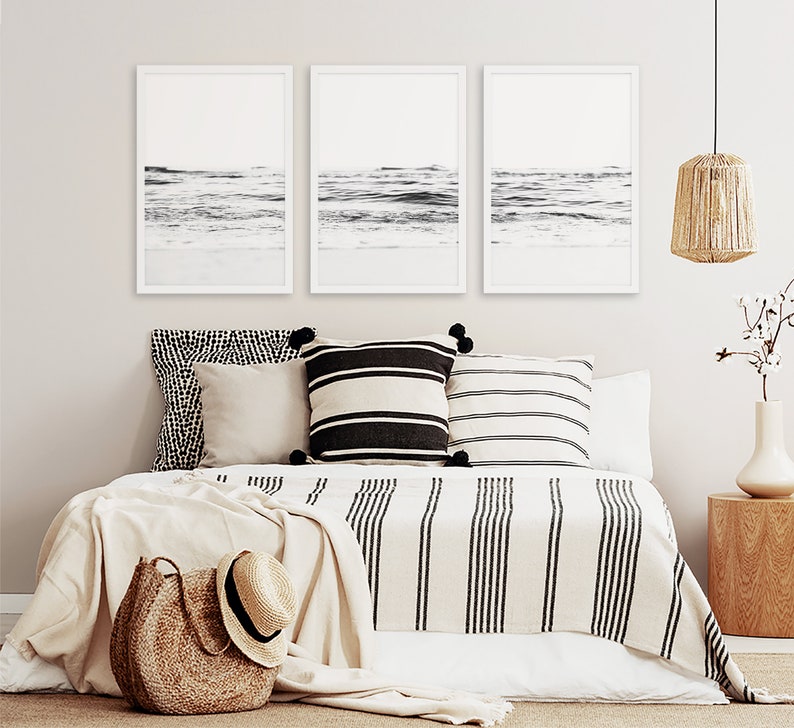 May include: Three black and white framed photographs of ocean waves hanging above a bed with a white and black striped blanket and pillows.