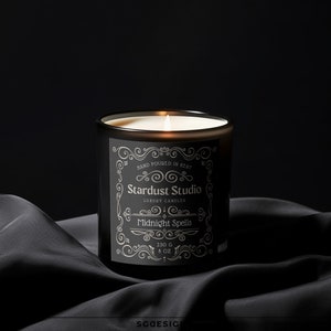 Puede incluir: Un tarro de vela negro con una etiqueta blanca que dice "Stardust Studio Luxury Candles Midnight Spells 230g 8 oz". La vela está encendida y la llama es visible.