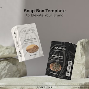 May include: Two soap boxes with a black and white design. The boxes are labelled "Lumina Luxe" and "Midnight Velvet Exfoliating Face Soap Bar". The boxes are floating in the air above a pile of rocks.
