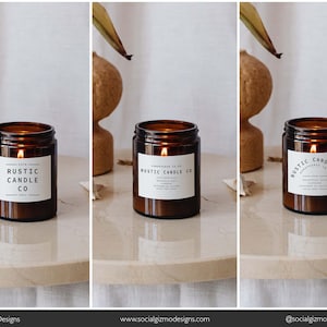 May include: Three amber glass candle jars with white labels that read "Rustic Candle Co." The candles are lit and the flames are visible. The candles are on a white marble surface.