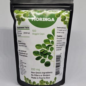 May include: A black resealable pouch with a white label that reads "MORINGA" in a green circle. The label also includes the product name, "Organic Moringa Extract (650mg)", "100 Veggie Caps", "650 mg", "Non-Gmo's Ingredients", "No Fillers or Binders", and "Made in Puerto Rico".