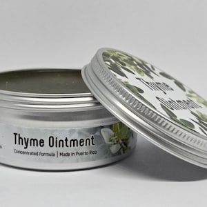 May include: A round silver metal tin containing Thyme Ointment with a concentrated formula. The lid features a green thyme leaf pattern and the text Thyme Ointment. The side label includes the text Thyme Ointment, Concentrated Formula, and Made in Puerto Rico.