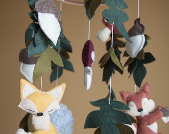 May include: A woodland-themed baby mobile with felt foxes, mushrooms, acorns, and leaves hanging from a wooden ring.