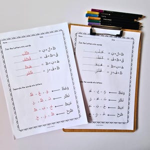 K&ouml;nnte beinhalten: Zwei Arbeitsbl&auml;tter mit arabischen Schreib&uuml;bungen, eines auf einem Klemmbrett. Die Arbeitsbl&auml;tter haben schwarzen und roten Text mit einem dekorativen Rand. Buntstifte liegen auf dem Klemmbrett.