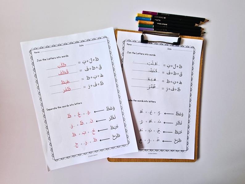 K&ouml;nnte beinhalten: Zwei Arbeitsbl&auml;tter mit arabischen Schreib&uuml;bungen, eines auf einem Klemmbrett. Die Arbeitsbl&auml;tter haben schwarzen und roten Text mit einem dekorativen Rand. Buntstifte liegen auf dem Klemmbrett.
