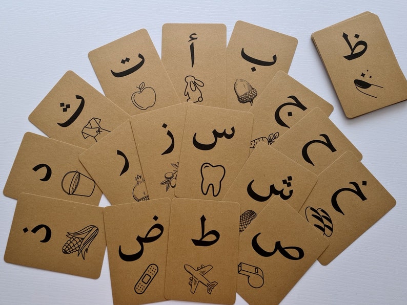 May include: A collection of flashcards with Arabic letters and corresponding illustrations in black ink on a brown cardstock. The images include an apple, a rabbit, an acorn, a tooth, and a bandage.