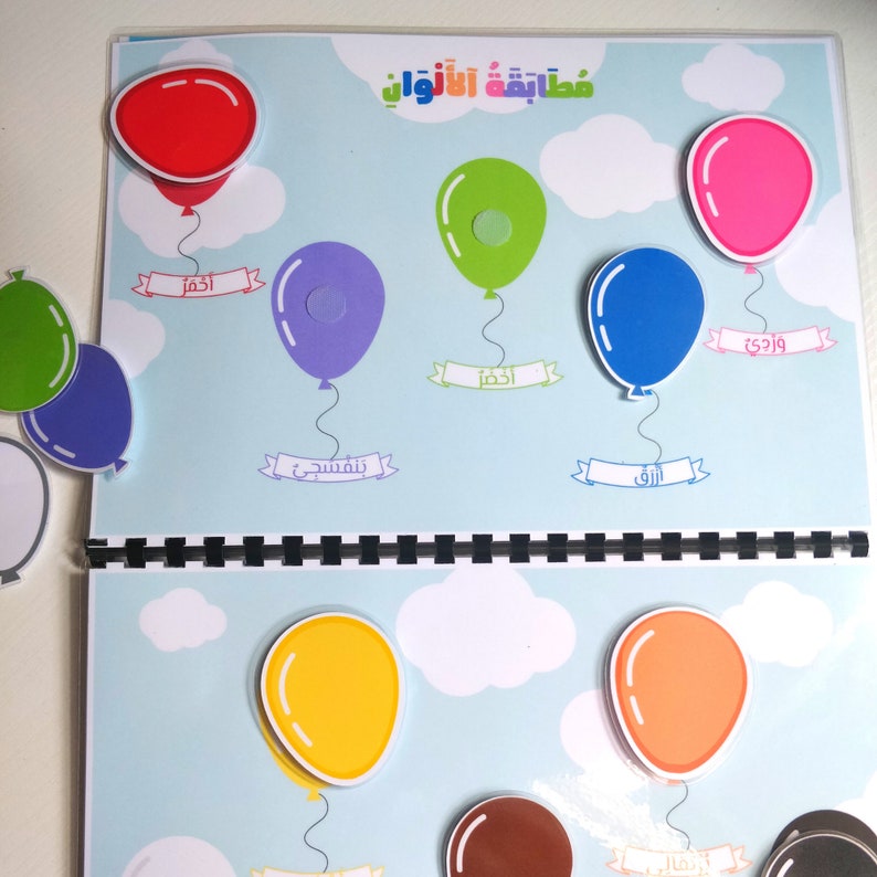 May include: A colorful educational learning book with balloon illustrations. The book features red, green, pink, blue, purple, yellow, orange, and brown balloons. Each balloon has a label in Arabic. The background is light blue with white clouds.