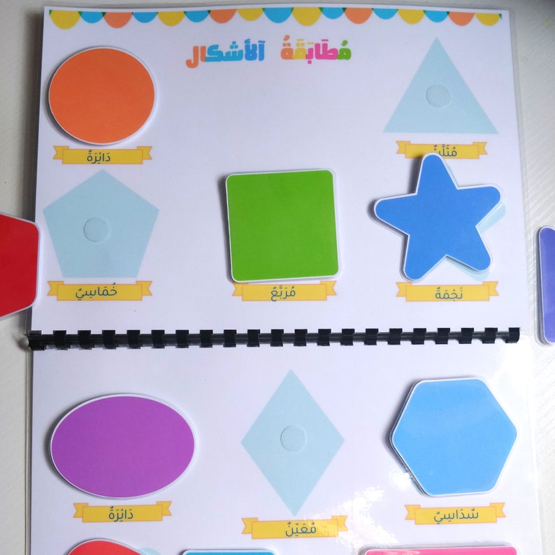 May include: A colorful educational book featuring various geometric shapes. The shapes include a circle, pentagon, square, triangle, star, oval, diamond, and hexagon. Each shape is labeled with text in Arabic. The book is bound with a black spiral.