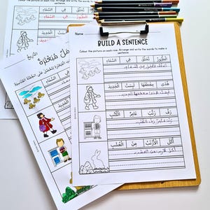 May include: A wooden clipboard holds worksheets with Arabic text and illustrations for sentence building. Colored pencils rest at the top. The worksheets feature drawings of a person, ducks, and a rabbit, with lines for writing sentences.