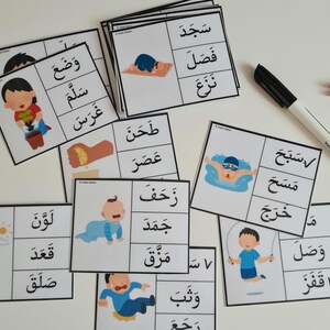 May include: A collection of flashcards with Arabic text and illustrations of children performing various actions. A black marker and colorful clothespins are also visible. The cards are designed for educational purposes.