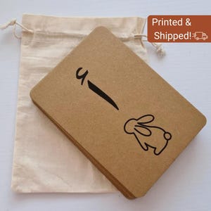 May include: A stack of brown rectangular cards with a black line and a bunny illustration. The cards are next to a beige drawstring bag. The text "Printed & Shipped!" is in a brown rectangle.