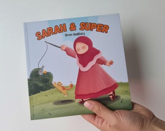Può includere: Un libro per bambini quadrato intitolato Sarah & Super di Sreen Haulkivory. La copertina presenta l'illustrazione di una persona con hijab e abito rosa che gioca con un gatto usando un giocattolo a forma di canna da pesca su un prato verde.