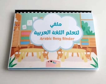 May include: A spiral-bound Arabic Busy Binder with a colorful cover featuring a classroom scene. The cover has Arabic text and the English text "Arabic Busy Binder" in a cloud-shaped design. The binder is on a white surface.