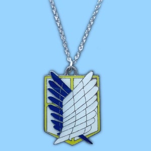 Op de afbeelding: Een zilveren ketting met een hanger met het Wings of Freedom-embleem uit de anime Attack on Titan. De hanger is geel, blauw en wit met een zilveren omtrek.