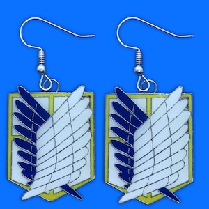 Puede incluir: Un par de pendientes de plata con un diseño de esmalte amarillo, azul y blanco de un símbolo alado.