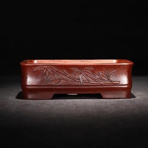 Può includere: Un vaso rettangolare per bonsai in terracotta rossa con un design di bambù intagliato.