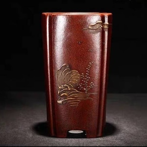 May include: A dark red ceramic planter with a gold design of a wave and a tree. The planter has a rectangular shape with rounded edges.