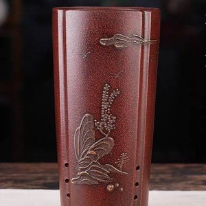 Może przedstawiać: Prostokątna doniczka z czerwonej gliny z dekoracyjnym wzorem przedstawiającym górę, drzewo i ptaka. Doniczka ma otwory drenażowe i kwadratową podstawę.