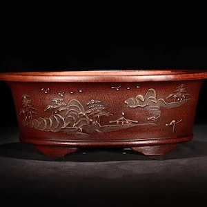 Könnte beinhalten: Ein roter ovaler Keramiktopf mit einem Landschaftsdesign in Gold. Der Topf hat drei Füße und ist perfekt für die Präsentation von Pflanzen.