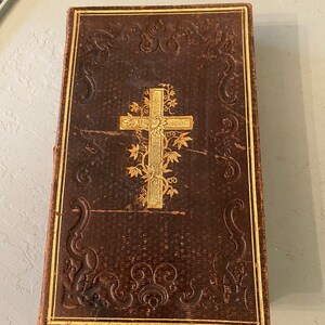 May include: A vintage brown leather-bound book with gold accents and a cross design on the cover.