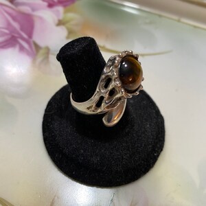 Könnte beinhalten: Ein silberner Ring mit einem braunen Tigerauge-Stein, der in einem dekorativen, verzierten Design gefasst ist.
