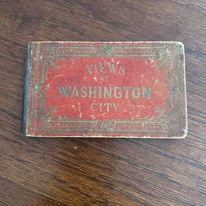 May include: A red book with gold lettering that reads "VIEWS of WASHINGTON CITY".