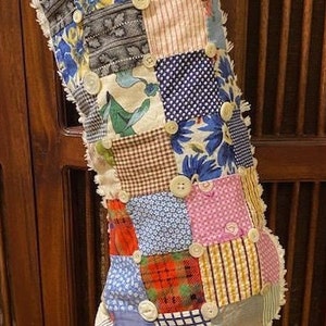 May include: A patchwork Christmas stocking with a blue, white, and brown color scheme. The stocking is made of various fabrics and has buttons sewn on it.