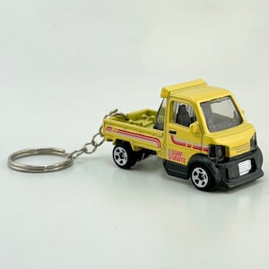 May include: A yellow toy truck with a black bed and a white "Surf Skate" logo on the side. The truck has a key chain attached to it.