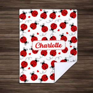 May include: White fleece blanket with a red and black ladybug pattern. The blanket has a personalized name, "Charlotte", in red text.