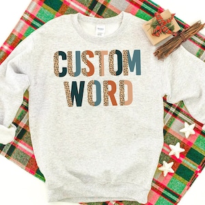 May include: A gray sweatshirt with the text "CUSTOM WORD" printed on the front. The letters are in a variety of colors and have a leopard print pattern.