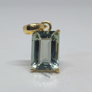 May include: A gold pendant with a light green emerald-cut gemstone. The pendant is on a white background.