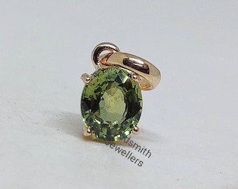 May include: A gold pendant with a round green gemstone. The pendant is on a white background.