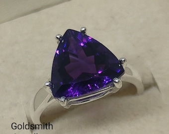 May include: A silver ring with a large, triangular, purple amethyst gemstone. The ring is in a white box with the text "Goldsmith Jewellers".