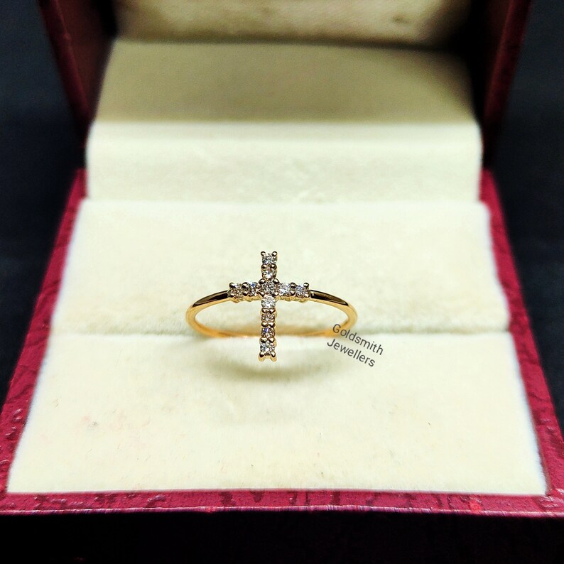 May include: A gold ring with a diamond-encrusted cross design. The ring is displayed in a velvet-lined box.