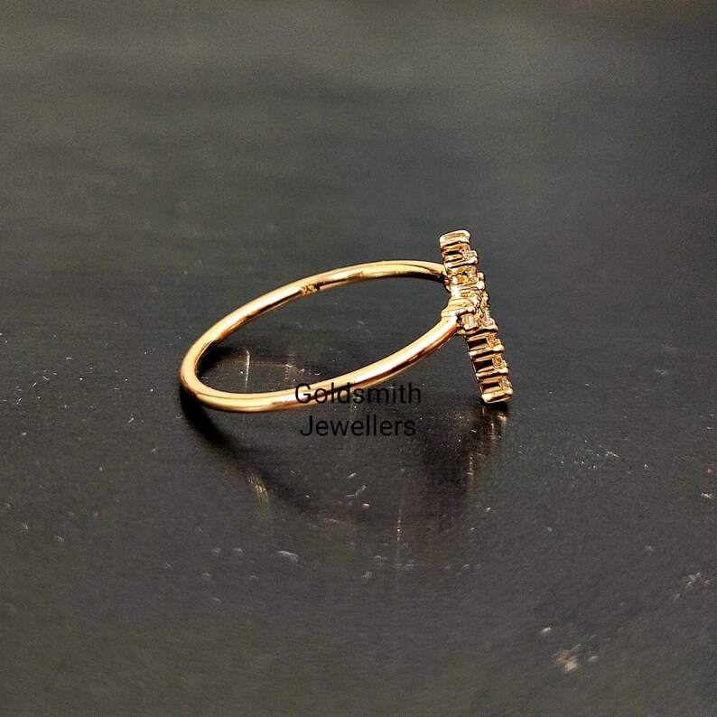 May include: A gold ring with a delicate band and a vertical design of small diamonds. The ring is set against a black background.