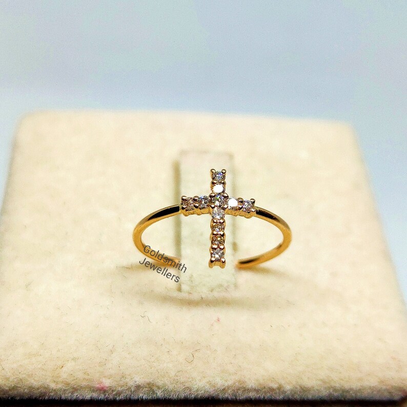 May include: A gold ring with a diamond-encrusted cross design. The ring is on a white background with the text "Goldsmith Jewellers".