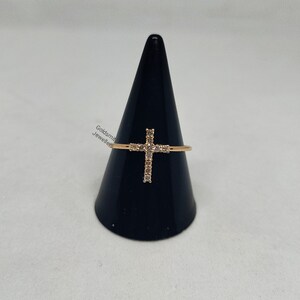 May include: A gold ring with a cross design set with clear cubic zirconia stones.