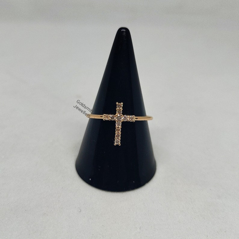 May include: A gold ring with a cross design set with clear cubic zirconia stones.