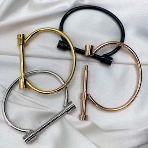 Könnte beinhalten: Drei Metallarmbänder mit einem einzigartigen Design. Die Armbänder sind golden, silber und schwarz.