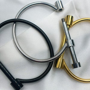 May include: Three metal bracelets with a simple, minimalist design. The bracelets are made of silver, gold, and black metal. Each bracelet has a small, round knob at the end.