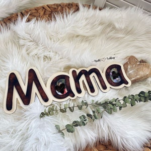 Könnte beinhalten: Ein Holzschild mit der Aufschrift "Mama" und zwei Herz-Ausschnitten für Fotos. Das Schild ist braun mit weißem Hintergrund und hat einen Used-Look. Der Text "Nuddl  Loving" ist in Kursivschrift über dem Schild geschrieben.