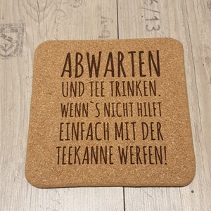 Könnte beinhalten: Ein Korkuntersetzer mit dem Text "ABWARTEN UND TEE TRINKEN. WENN'S NICHT HILFT EINFACH MIT DER TEEKANNE WERFEN!" in brauner Schrift.