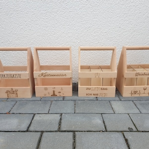 Peut inclure: Quatre caisses en bois avec des poignées, chacune avec un design et un texte gravés différents. Les caisses sont étiquetées "Werkzeugkiste", "Küstenwasser", "Zu Wein Sag Ich Nie Nein", et "Weinbuddy".