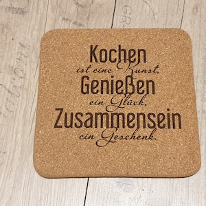 Può includere: Un sottobicchiere di sughero con il testo "Kochen ist eine Kunst, Genießen ein Glück, Zusammensein ein Geschenk."