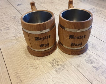 Op de afbeelding: Twee houten bierbekers met metalen banden en handvatten. De bekers zijn gegraveerd met de tekst "Bester Opa" en "Bester Papa".