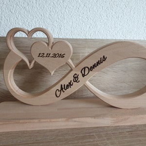 May include: A wooden infinity symbol with two hearts intertwined. The hearts are carved with the date "12.11.2016" and the text "Alex & Dennis" is engraved on the infinity symbol.